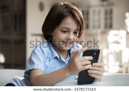 Close up smiling Caucasian boy using smartphone at home, sitting on couch alone, curious adorable 7s child kid looking at phone screen, playing games or watching cartoons, video, leisure time