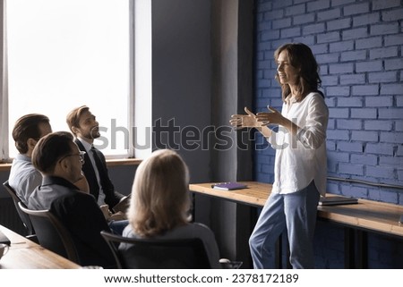 Attractive young company speaker talk to different ages employee on business meeting, help defines task and corporate goal. Teammates group discuss work on project in boardroom. Brainstorm, leadership Royalty-Free Stock Photo #2378172189