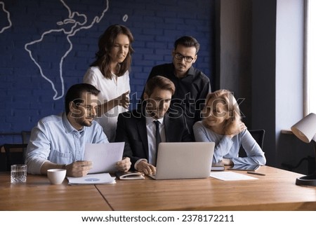 Different ages colleagues analyze data looks at laptop screen, watch presentation, discuss new ideas for project, brainstorming. Businesspeople solve work issues together in office. Strategy, teamwork