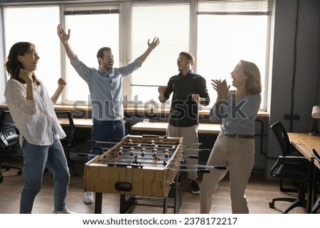 Cheerful euphoric young and mature colleagues playing table soccer at lunch break, having fun, scream with joy, celebrate victory, feel overjoyed, excited, enjoying competition, teambuilding activity Royalty-Free Stock Photo #2378172217