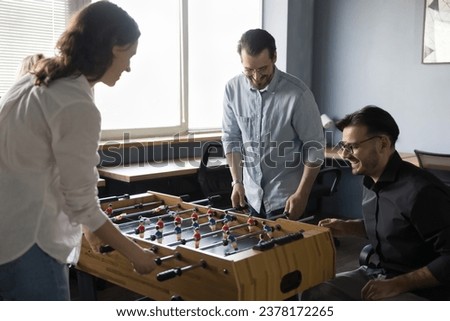 Happy joyful teammates, friendly colleagues having fun at workplace. Group of cheerful employees playing table soccer during lunch break, gathered together laughing, enjoy tabletop football in office Royalty-Free Stock Photo #2378172265