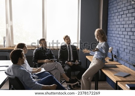 Middle aged woman leader stand in office explain work task, discuss project, present new creative idea or plan. Positive older coach gives seminar to young employees, Teambuilding, mentoring, business Royalty-Free Stock Photo #2378172269