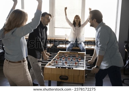 Cheerful businesspeople, teammates play table soccer in office during break. Group of coworkers having fun distracted from work, competing in toy tabletop football game, laughing, cheering, supporting Royalty-Free Stock Photo #2378172275