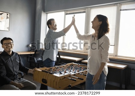 Joyful male female coworkers enjoying teambuilding activity, having fun, playing table football, clapping hands, give high five gesture over boardgame, win battle, congratulate each other, finish game Royalty-Free Stock Photo #2378172299