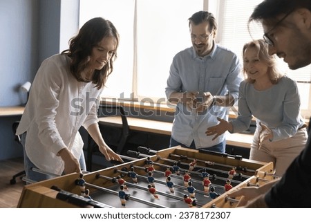 Four positive diverse older and younger employees engaged in foosball game in modern office, play together tabletop soccer indoors, spend carefree break at workplace. Hobby, teambuilding activity, fun Royalty-Free Stock Photo #2378172307