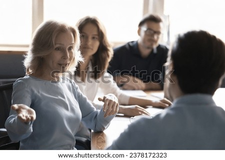 Mature woman talking to businessman at corporate meeting in office, gathered in office to planning joint project, businesspeople discuss work moments, share new ideas. Partnership, business, briefing Royalty-Free Stock Photo #2378172323