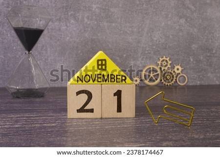 Calendar for November 21: name of the month in English, number 21, birch branch with one yellow leaf, fallen birch leaves on a wooden table, gray background, rays of the sun