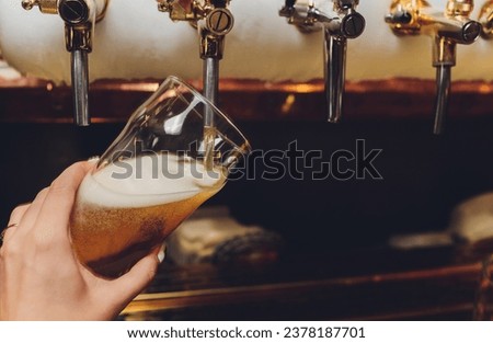 Barkeeper pulling a pint of beer behind the bar Royalty-Free Stock Photo #2378187701