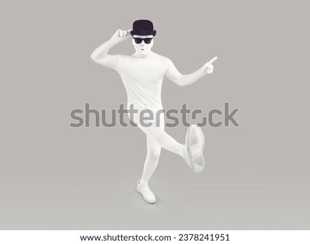 Funny disguised dancer in studio. Full length portrait of man in white bodysuit costume, mask, black bowler hat and sunglasses dancing and pointing index finger away isolated on grey color background Royalty-Free Stock Photo #2378241951