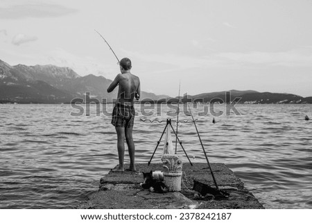 Boy and cat fishing at sea dock. Black and white photography.