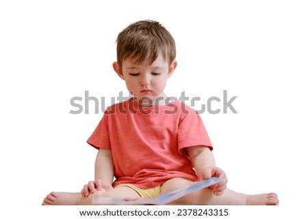 The cute baby is playing with the colorful picture book, flipping through the pages and touching the pictures, isolated on white background. The little child is lost in thought as he reads book