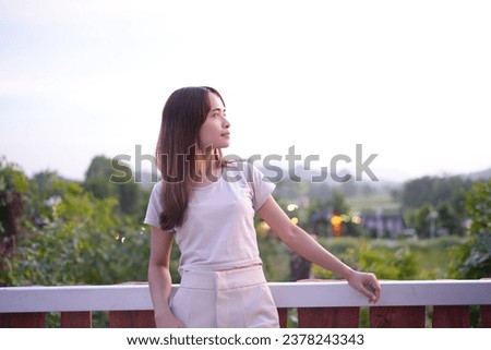 Happy Asian female tourist taking photos on the roof of her accommodation during sunset.
