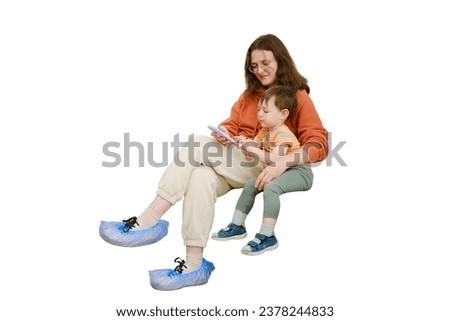The baby and his mother are sitting together in the hospital hall, playing a game on their phone to pass the time before their doctor's visit, isolated on white background. Kid boy aged two years