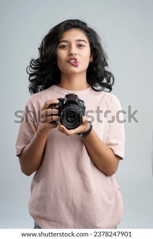 A girl playfully forms a heart shape with her lips while cradling a camera, capturing moments of love and joy.