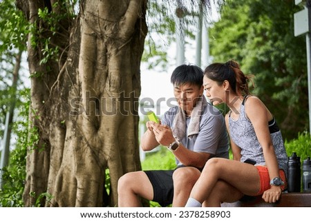 young asian couple looking at cellphone while taking a break during outdoor exercise