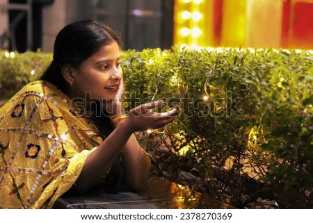 Indian girl smiling in front of light decorated plant for diwali