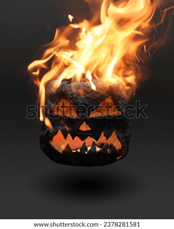 Burning black dry halloween pumpkin smile and scary eyes for party night. Close-up of a scary Halloween pumpkin on fire with glowing eyes on a black poster background. Selective focus.