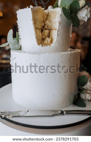 A large, beautiful, two-tier, decorated with fresh flowers, roses, white wedding cake, cut with a knife, stands on the table in the restaurant. Food photography, dessert concept. Royalty-Free Stock Photo #2378291703