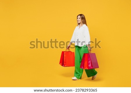 Full body young woman wearing white casual clothes hold in hand paper package bags after shopping walking go isolated on plain light yellow color background studio. Black Friday sale buy day concept