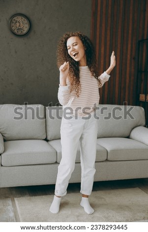 Full body happy young woman wear casual clothes stand near grey sofa couch sing song pov in microphone stay at home hotel flat rest relax spend free spare time in living room indoor. Lounge concept