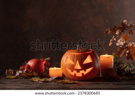 Halloween pumpkin head jack lantern with dried-up leaves. Halloween holidays art design, celebration. Carved Halloween pumpkin with burning candle.