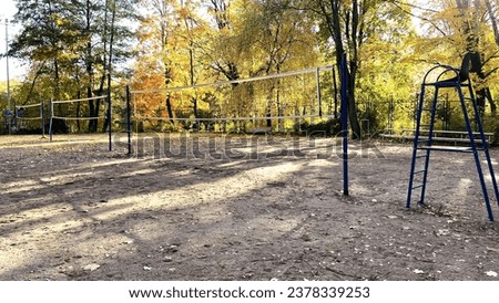 An empty sports volleyball court in the city park in autumn, it's autumn outside, they don't play volleyball, there are no people, it's cool, yellow trees on the background of a volleyball net