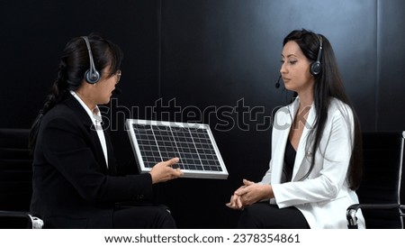 asian master of ceremonies or journalist in suit giving interview to businesswoman or celebrity with solar cell to renewable energy power energy and eco environment concept in  studio tv show on air 