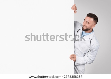 Cheerful male doctor playfully peeking from behind large blank white board, ready for personalized text or graphics, dressed in white coat with stethoscope, free space, banner