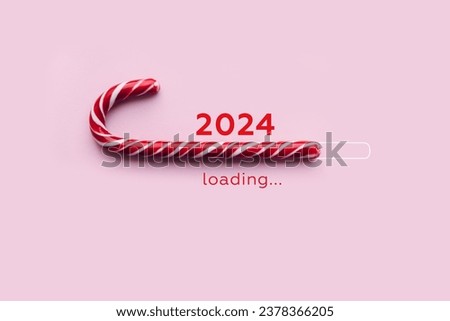 Striped candy cane and lettering 2024 loading on pink background. Concept of waiting for seasonal holidays. Copy space, selective focus