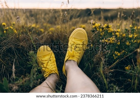 Female legs in sneakers lieing on flower blooming meadow, in countryside outdoor, in the field on summer day in meadow, feel the nature, relax, alone travel