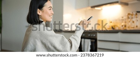 Close up portrait of smiling asian woman watching television, sitting on sofa with remote and switching chanel, looking relaxed.