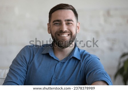 Cheerful confident handsome adult man sitting on couch, armchair at home against white wall background, looking at camera, smiling. Happy homeowner, blogger, freelancer head shot portrait Royalty-Free Stock Photo #2378378989