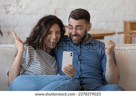 Happy excited adult dating couple using smartphone, staring at screen, getting great surprising good news, winning prize, celebrating success, achieve, fortune, laughing, making winner gesture Royalty-Free Stock Photo #2378379025
