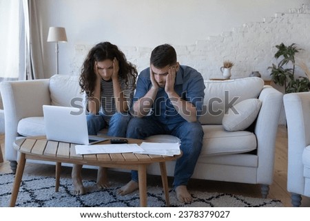 Concerned worried married couple getting financial problems, money crisis, counting overspent budget, high mortgage, rental fees, holding heads, looking at paper bills at home Royalty-Free Stock Photo #2378379027