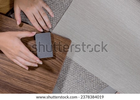 An interior designer's hand selects a palette of sample materials that includes different types, textures and colors of artificial stone, wooden MDF board and decorative wallpaper. Royalty-Free Stock Photo #2378384019