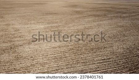 The aerial shot highlights the textured pattern of a plowed farm field against the solid black soil.