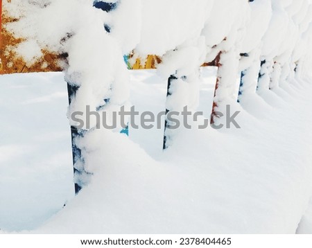 Close-up of diminishing perspective photograph of a snow-covered colorful wooden garden fence on a winter day. Royalty-Free Stock Photo #2378404465