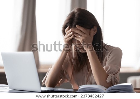 Frustrated stressed woman sit at desk near laptop hold head with hands feels desperate about dismissal, received bad news from bank business e-mail, personal life troubles, overworked headache concept Royalty-Free Stock Photo #2378432427