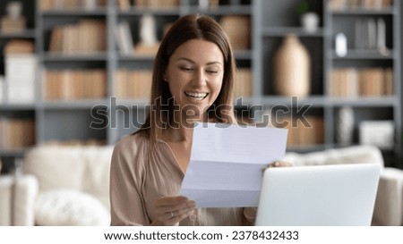 Smiling woman reading positive business letter, holding document with good news while sitting at home or modern cozy office desk, housewife got loan approval notification from bank, got job concept Royalty-Free Stock Photo #2378432433