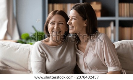 Cheerful elderly mother hugs adult 30s daughter different ages and generations women laughing seated on couch at home, enjoying communication, remembering past funny stories, sharing news, feels happy Royalty-Free Stock Photo #2378432439