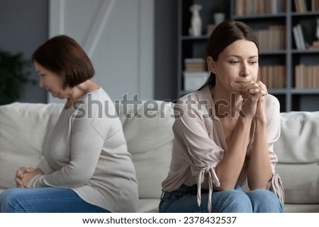 Frustrated adult daughter seated on couch with middle-aged sad mother women not looking talking after quarrel, concept of different opinions and outlook on life, generational gap, spoiled relations Royalty-Free Stock Photo #2378432537