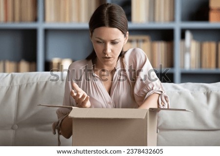 Woman sitting on couch put on lap carton box opened it feels disillusioned parcel arrives damaged broken or mixed up goods, negative feedback, wrong order, bad product quality, return refund concept Royalty-Free Stock Photo #2378432605