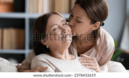 Loving adult daughter kisses her middle-aged mother on cheek, different generation beautiful women closed eyes enjoy meeting and tender moment, unconditional love attachment, strong connection concept