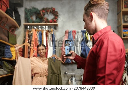 Young man photographing girlfriend with two dress for her blog