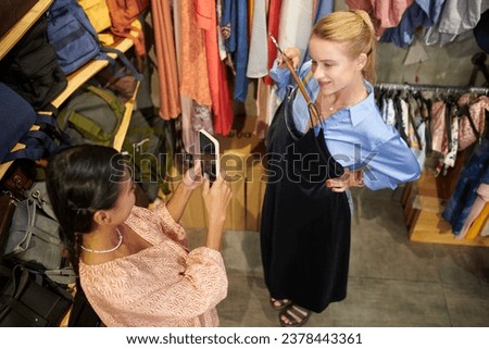 Young woman photographing friend trying on black velvet dress