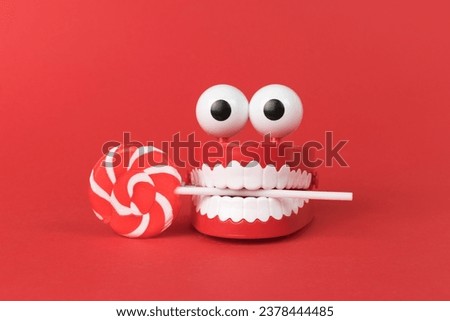 A wind-up toy with teeth and eyes with a lollipop on a red background. The concept of a holiday and parties.