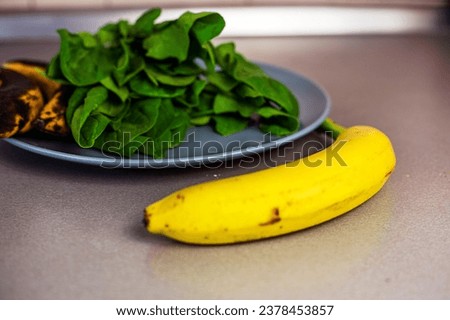 banana lies on the counter next to a plate of spinach and two overripe bananas