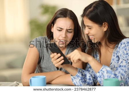 Two friends watching funny media content on phone at home Royalty-Free Stock Photo #2378462877