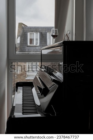 Glass of red wine placed on black piano by the window that looks out onto the brick house outside. Living room interior, Space for text, Selective focus