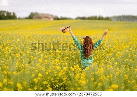 Happy woman is having fun and walking in a blooming rapeseed field. A beautiful woman in a bright dress and hat enjoys the sunny weather. Concept of nature, relaxation.